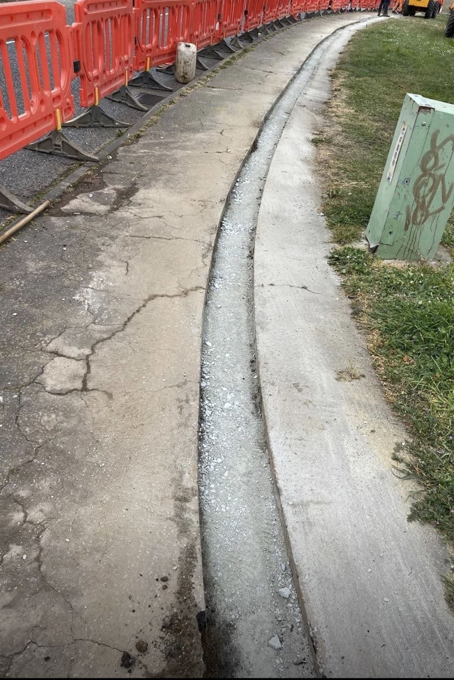 Narrow fibre optic trench cut along a concrete footpath under traffic management