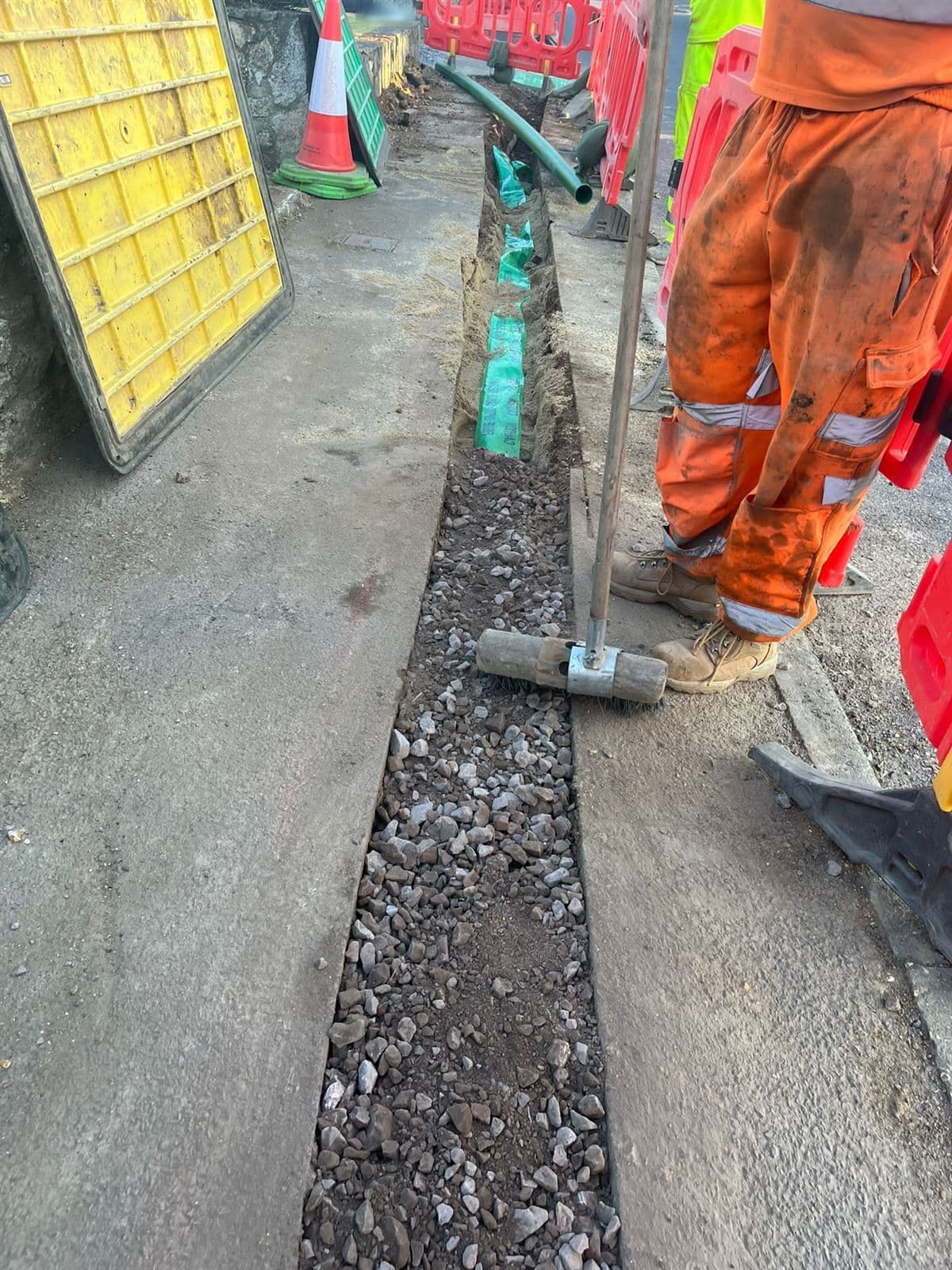 Utility trench backfilled with compacted Type 1 stone over green marker tape